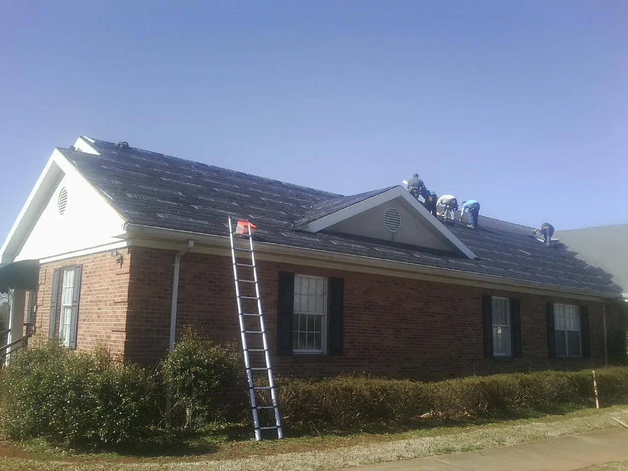 Crew tearing shingles off a brick ranch roof with a ladder set — Emergency Roof Repair work by our crew in Wellington